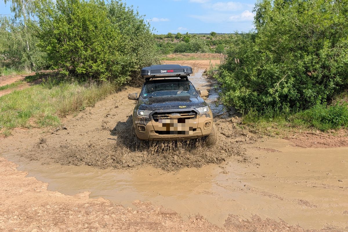 Ford Ranger Doppelkabiner mit Dachzelt fährt durch eine schlammige Offroad-Passage