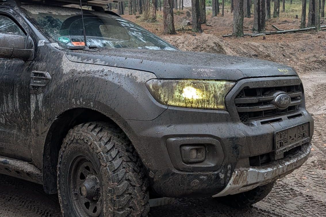 Verschlammter Ford Ranger Wildtrak mit Dachzelt auf einem Sandweg im Kiefernwald in Polen