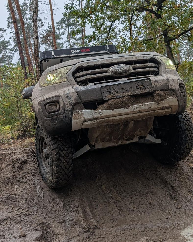 Ford Ranger fährt durch eine steile, schlammige Passage im Wald, Blick von unten auf die Front